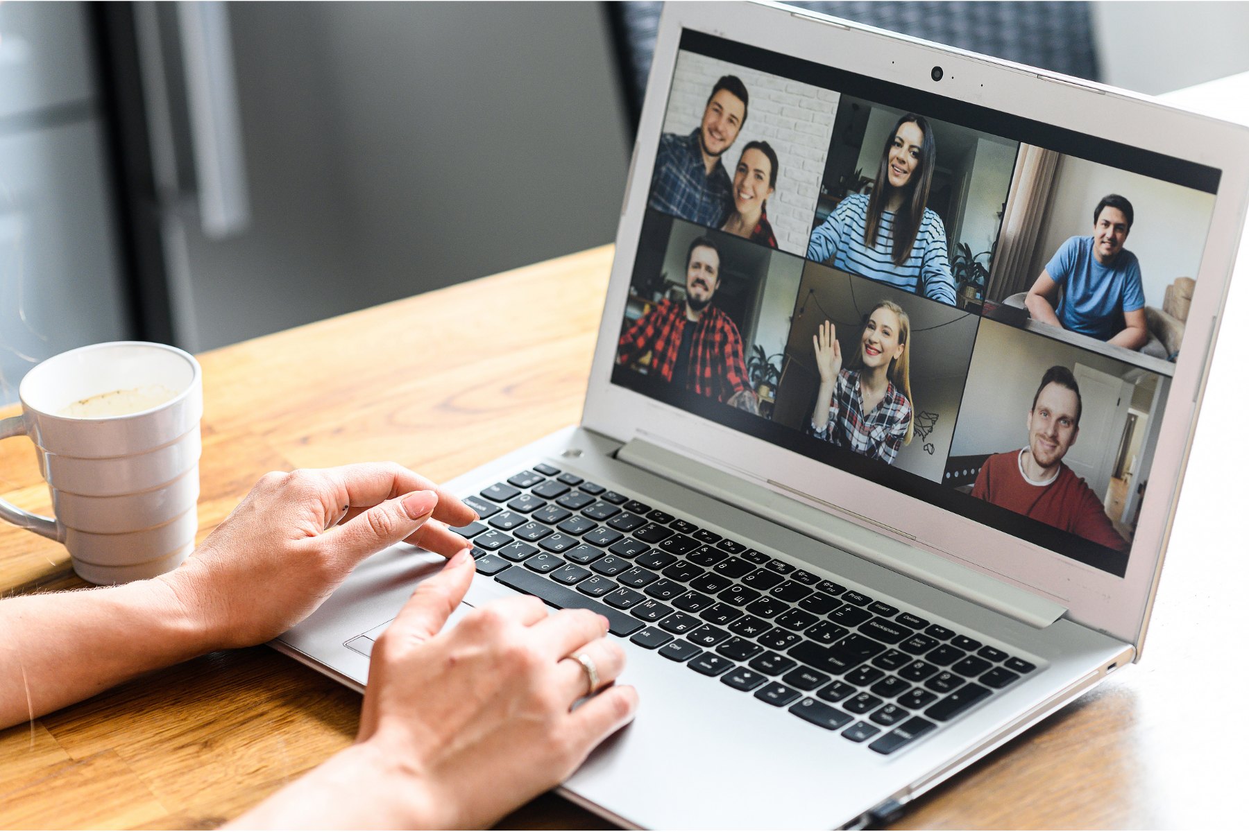 A laptop screen showing a grid of participants on a video call, with a coffee cup nearby