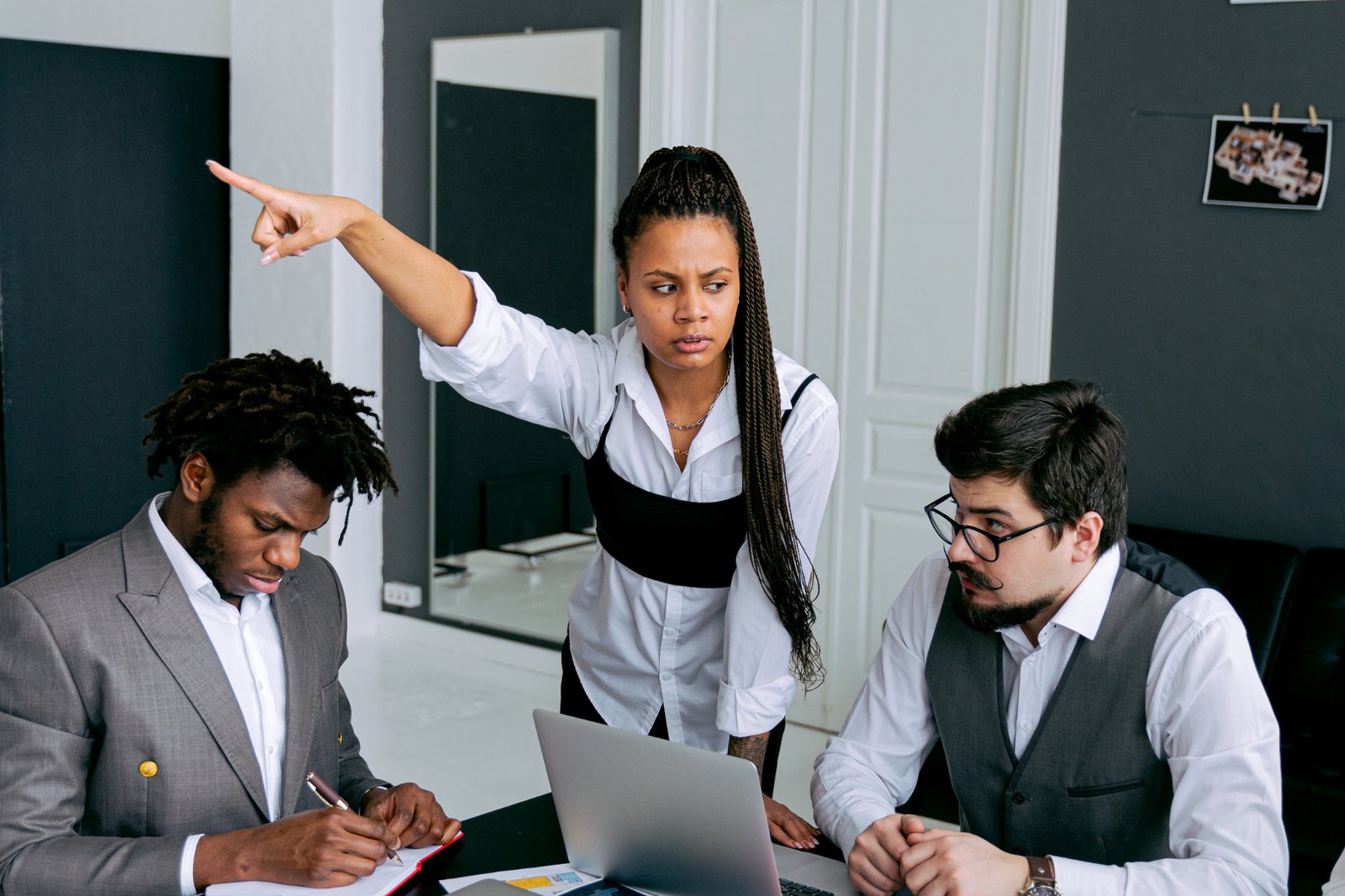 A frustrated manager pointing while two colleagues sit at a table
