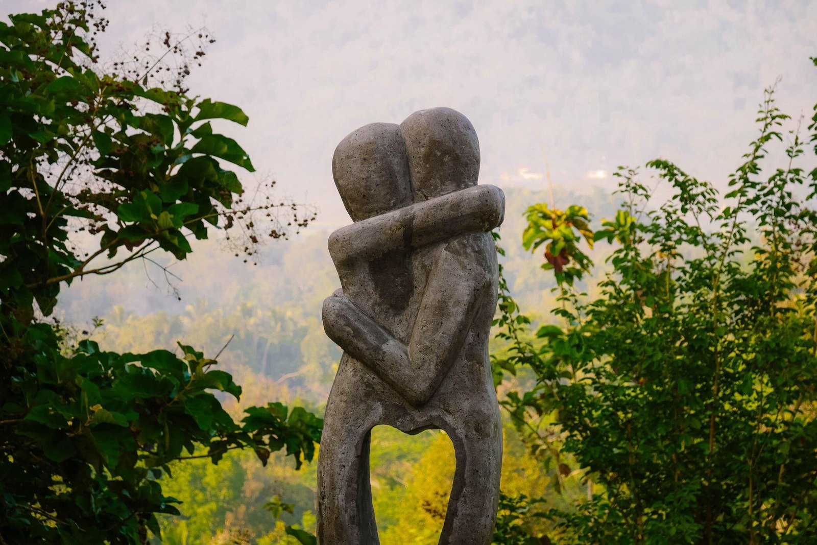 A stone sculpture of two figures embracing, surrounded by lush greenery