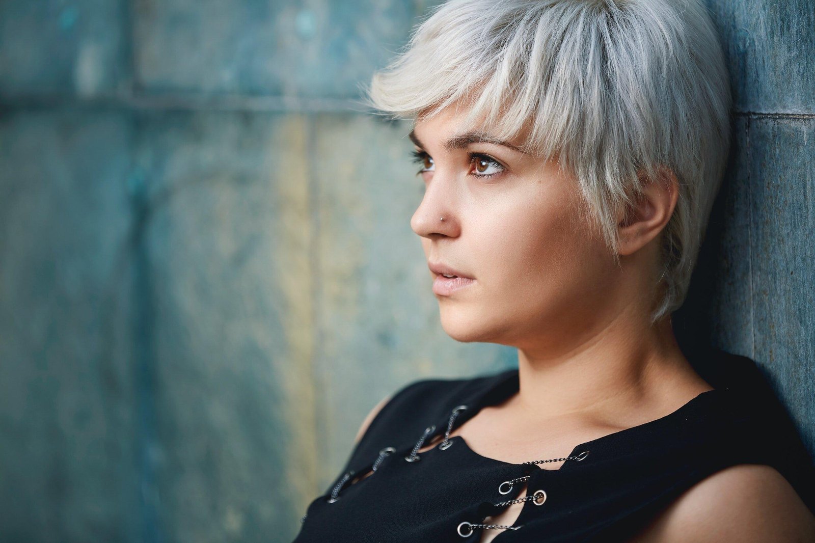 A woman leaning against a weathered blue wall, lost in thought