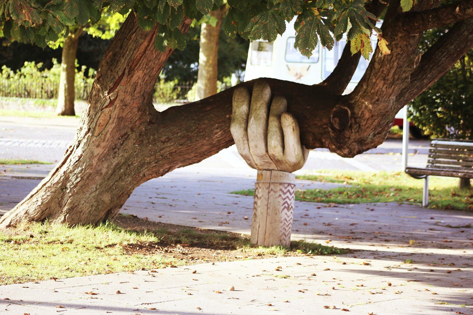 A carved wooden hand holding up the leaning trunk of a tree