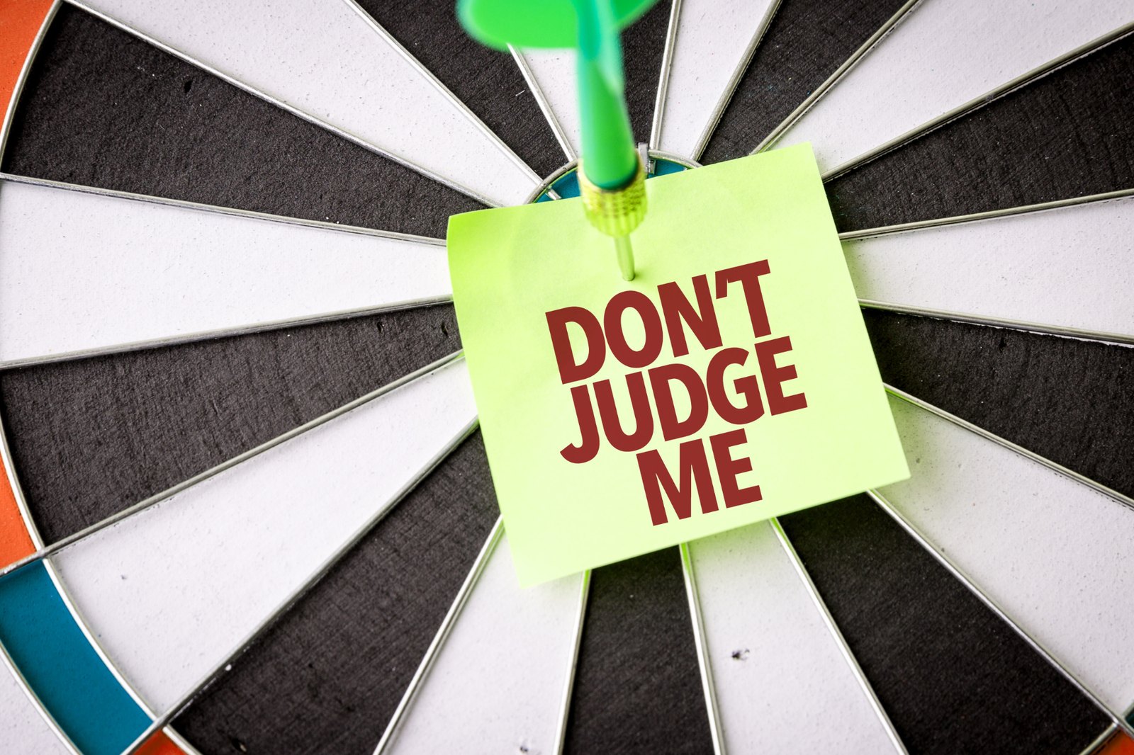 A sticky note reading Don't Judge Me pinned to the center of a dartboard