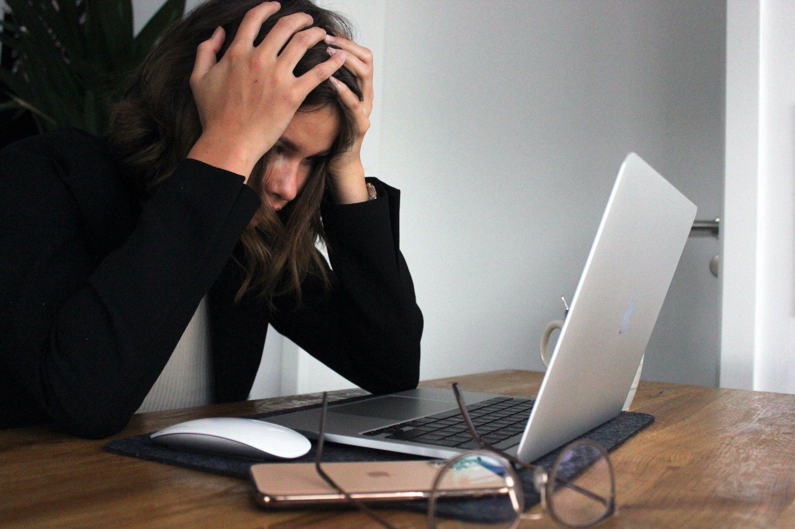 A stressed woman holding her head in her hands in front of her laptop