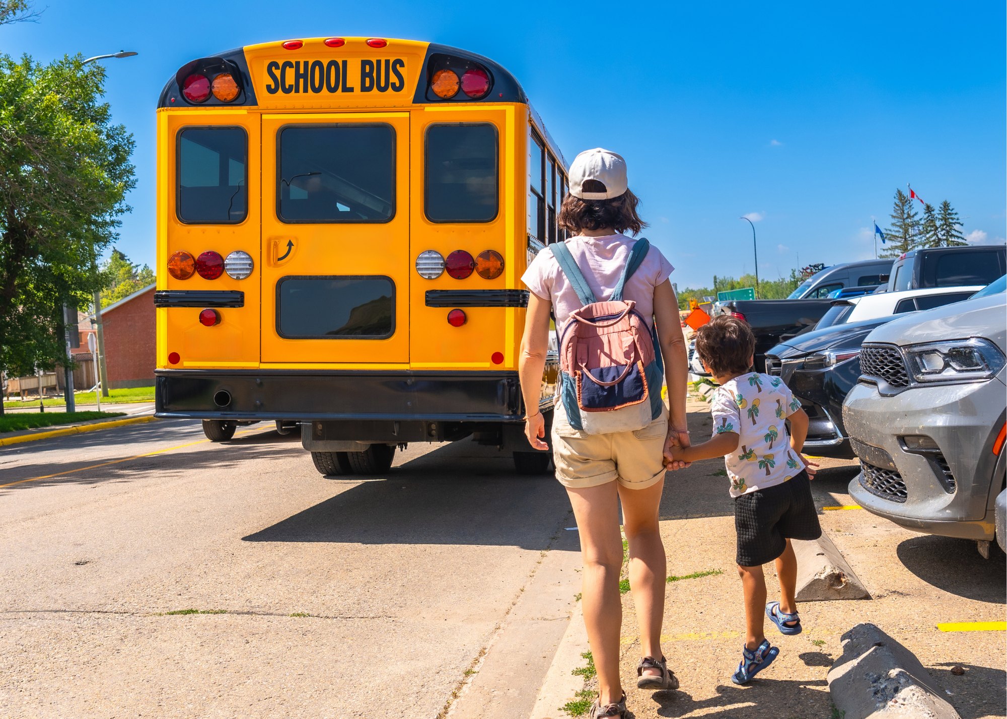 A parent holding a child's hand as they walk toward a school bus on a sunny morning